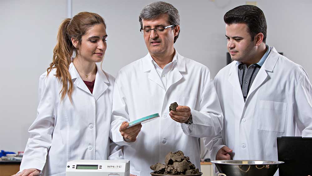 一个女人和两个穿着实验室工作服的男人在测量一些棕色的东西