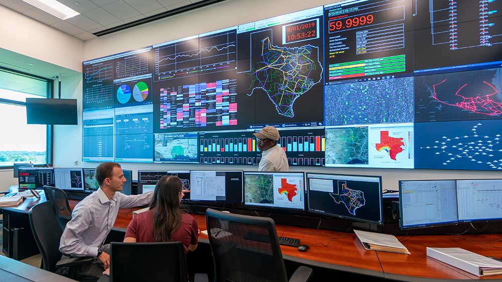 满屋子的显示器和墙上的屏幕显示着德克萨斯州的数据，一男一女坐在电脑前，另一个男人看着他们。