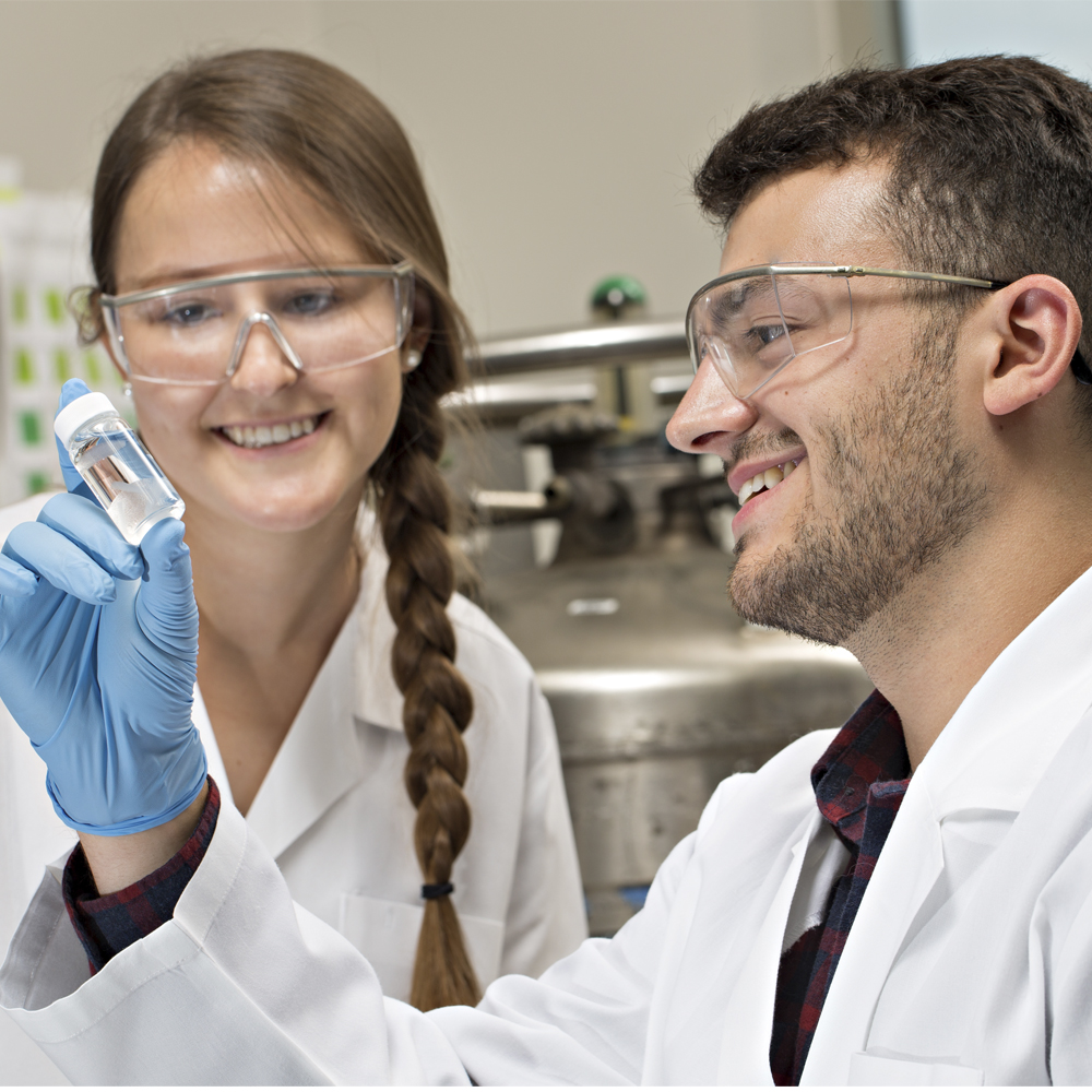 两名学生，一男一女，看着装满材料的小瓶子。他们在实验室里。