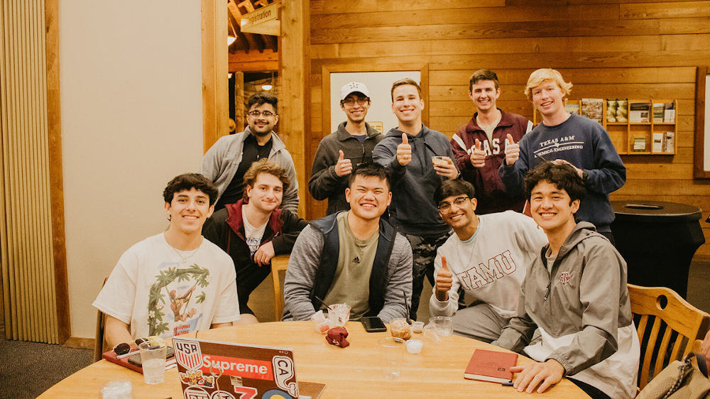 一群男学生围在一张桌子旁，微笑着摆姿势拍照。
