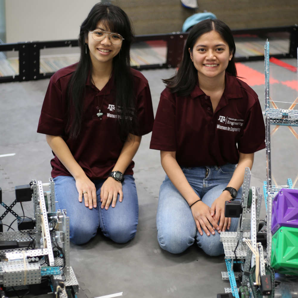 两名女工程师坐在两个机器人后面的地上