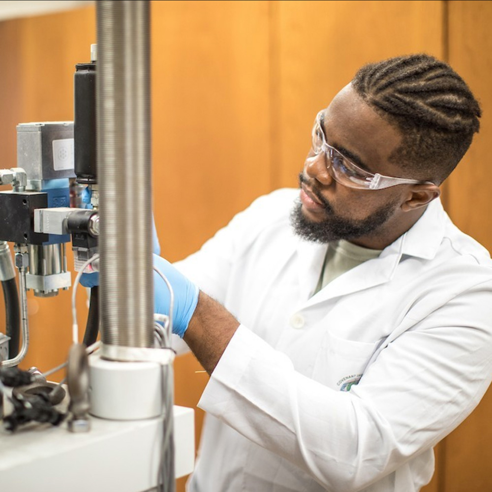 Student in lab coat and gloves working with machinery