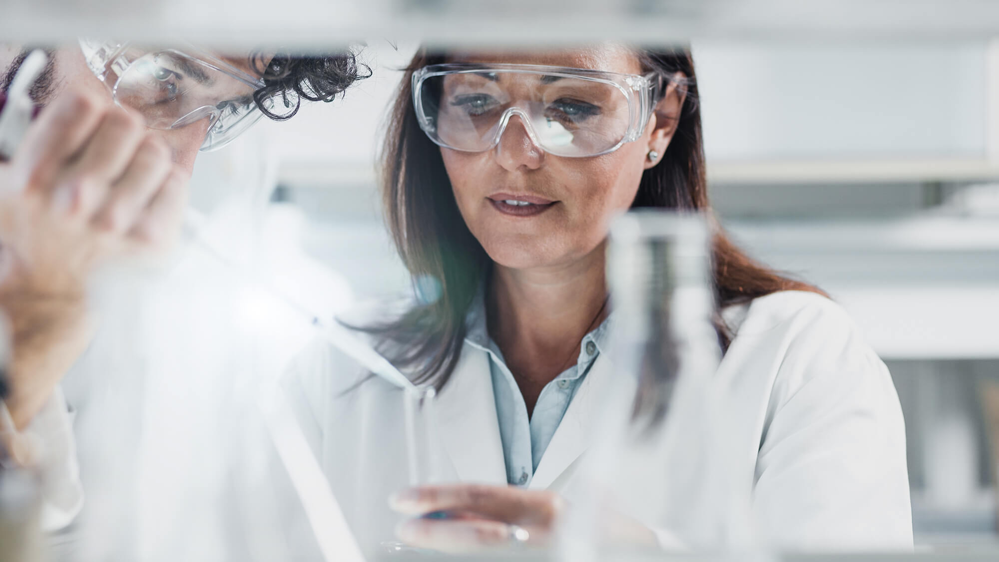 Woman engineering in white coat pours substance into beaker