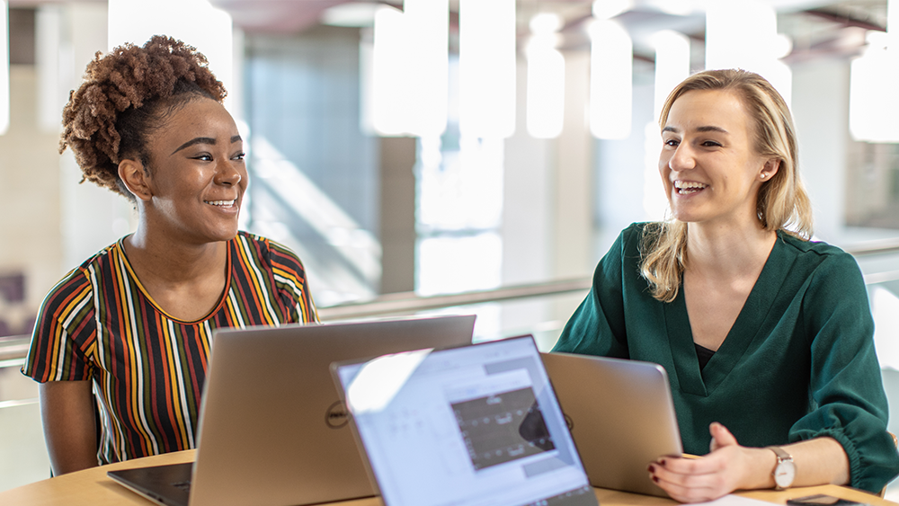 Two women laugh and smile as they work on computers