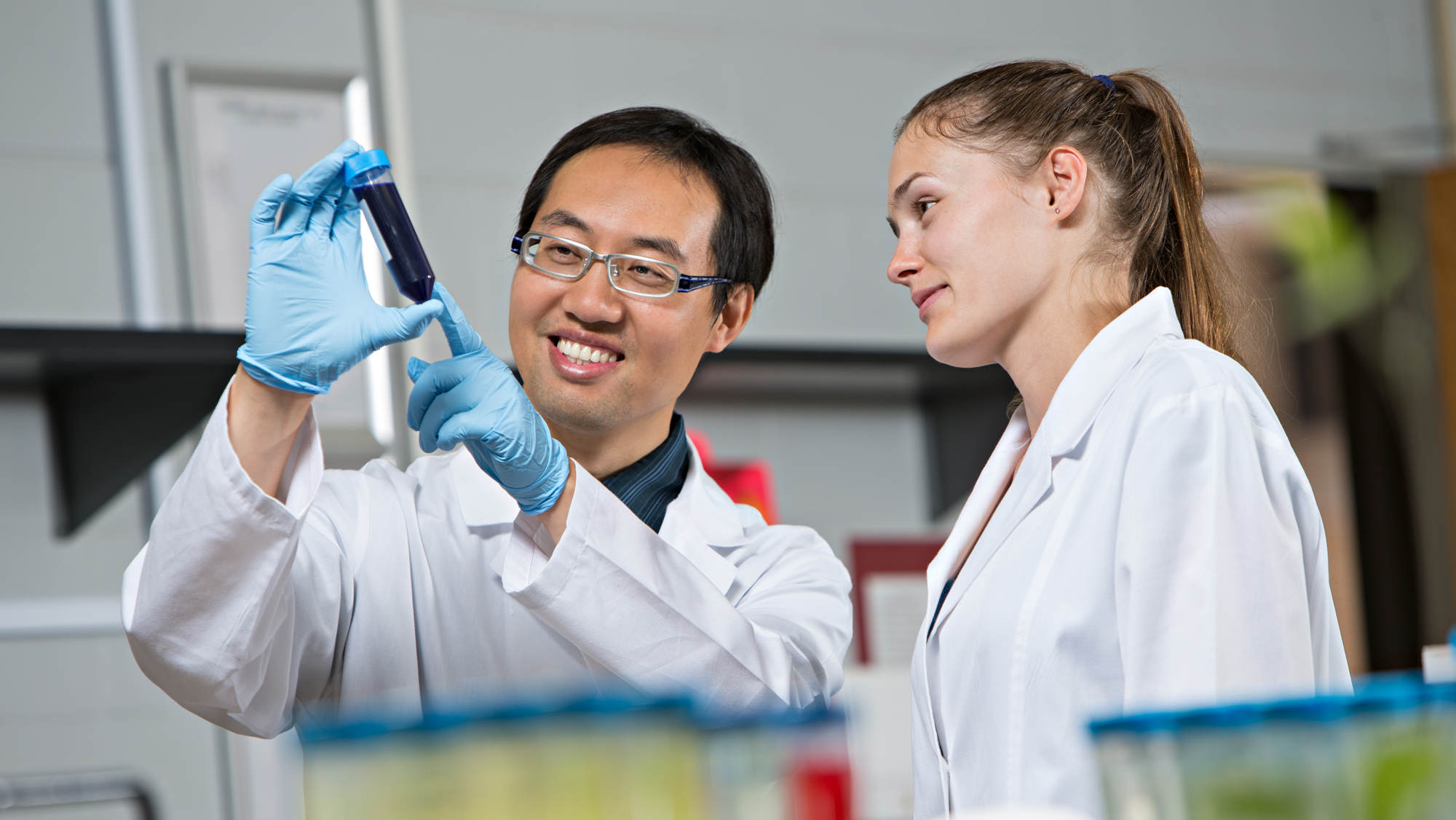 A faculty member holding a test tube and a student in white lab coats