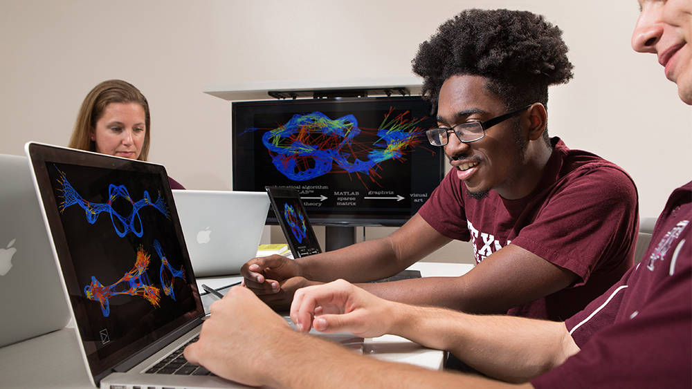 Image of two students looking at a colorful image on a laptop.