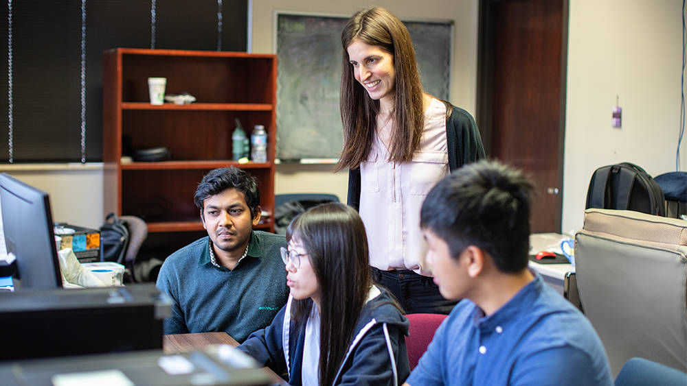 Image of professor and students looking at a laptop.