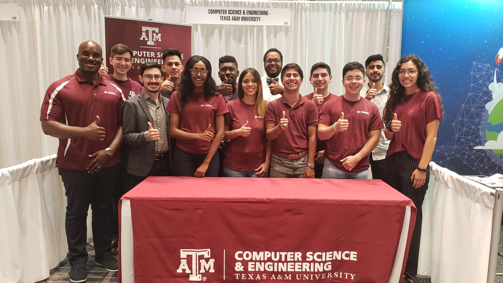 David Kebo博士和一组12名男女学生微笑着做着“gig 'em”的手势。