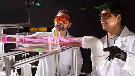 Two nuclear scientists in lab coats look at an experiment.