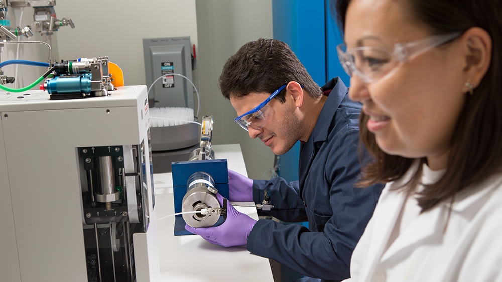 two graduate students, one male and one female, dressed in safety attire working with equipment in a Texas A&M petroleum engineering lab