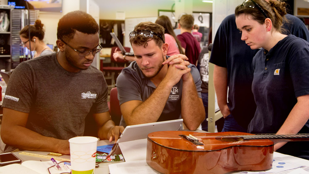 Three students working on a design challenge involving music and a guitar.