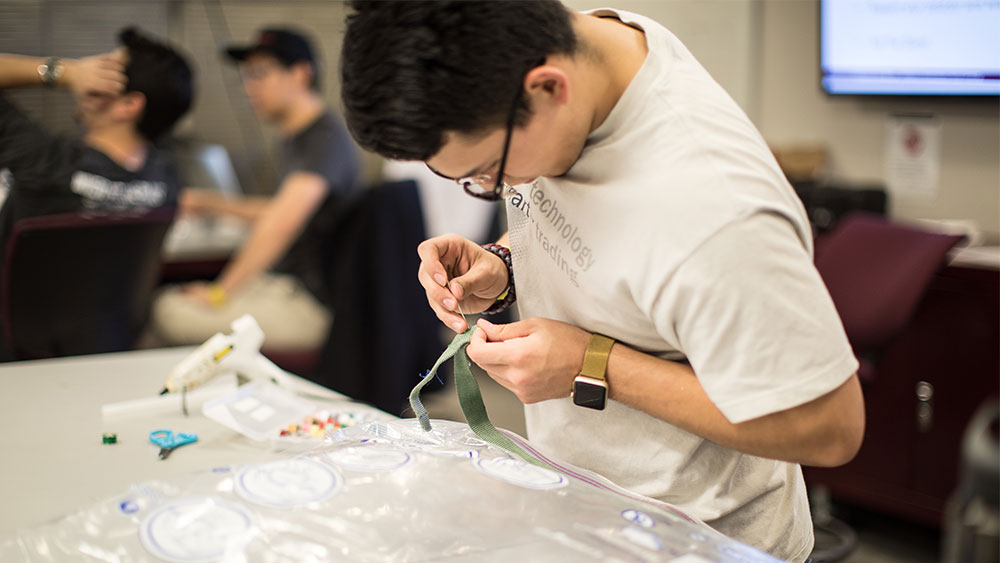 Male student sewing arm band for product development.