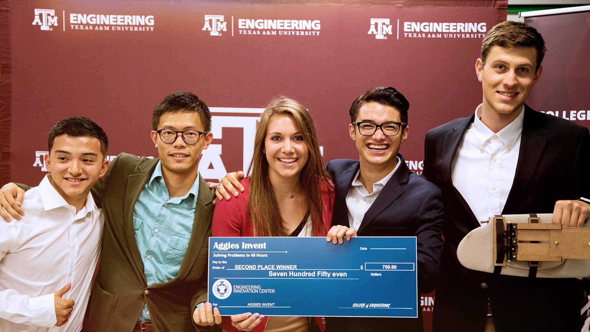 Texas A&M University Engineering 5 student holding each others shoulders their project and a check Aggies Invent Solving Problems in 48 hours pay to the order of Second Place Winner Seven Hundred and Fifty Even Dollars Engineering Innovation Center.